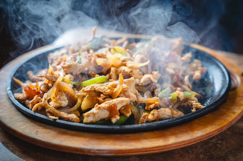 Chicken fajitas smoking on a cast-iron skillet