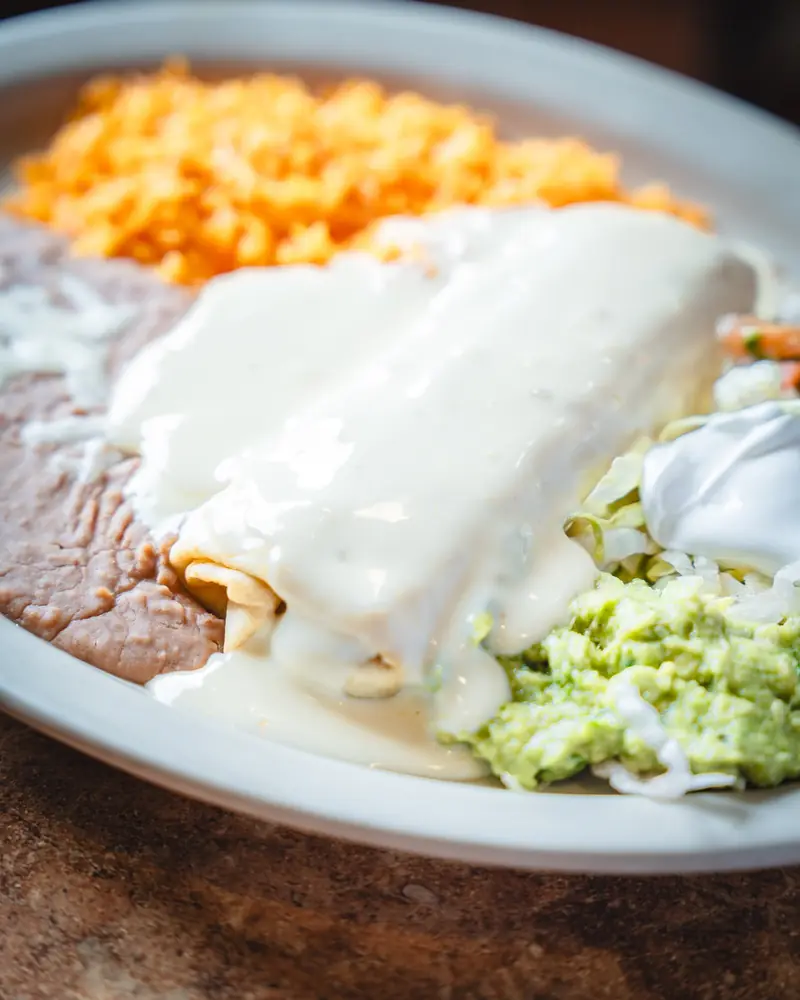 Chimichanga smothered in cheese sauce with rice, beans, guacamole and sour cream