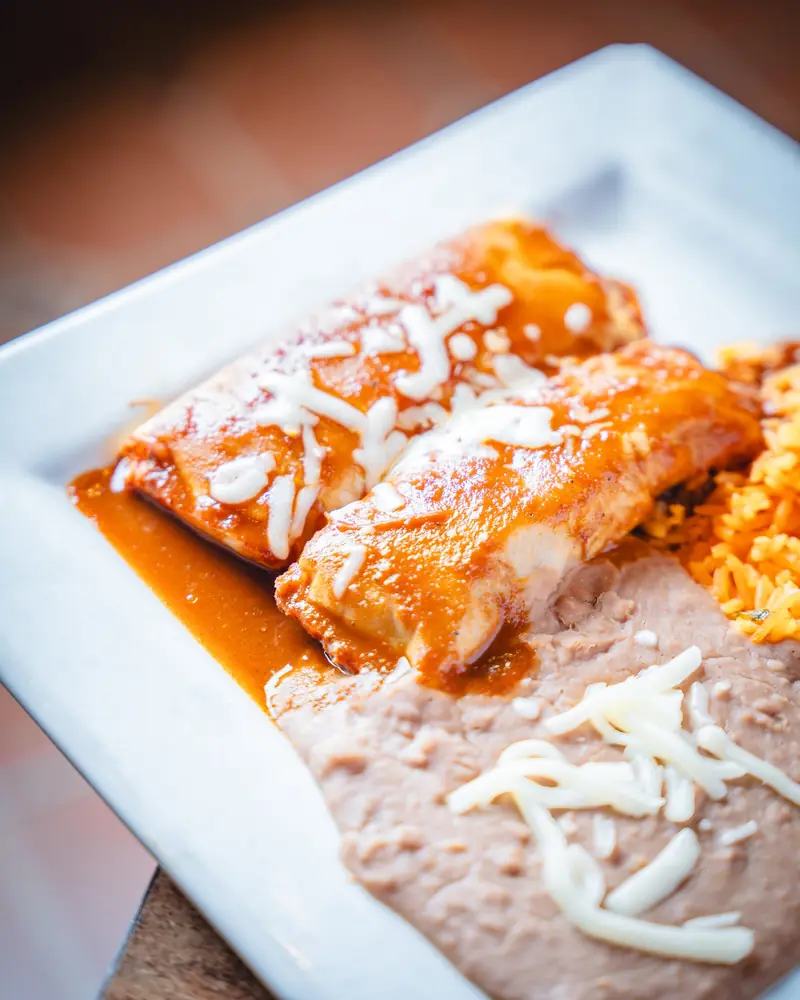 Tamales in red sauce with shredded cheese, rice and refried beans